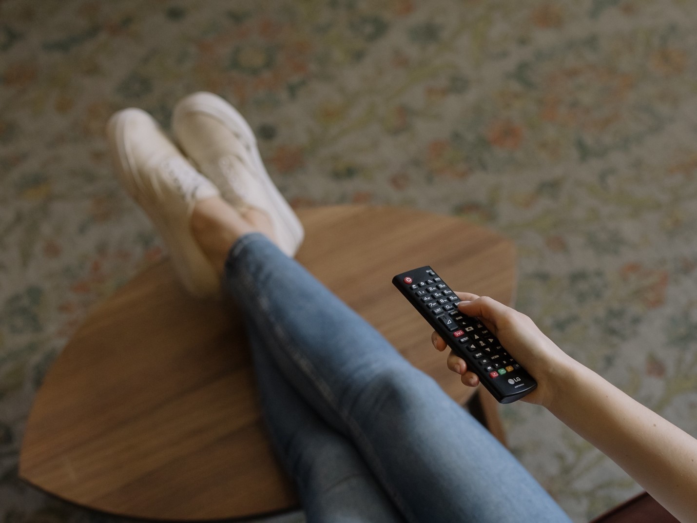 An overhead shot of a woman with her feet up on a coffee table and a TV remote in her hand. 