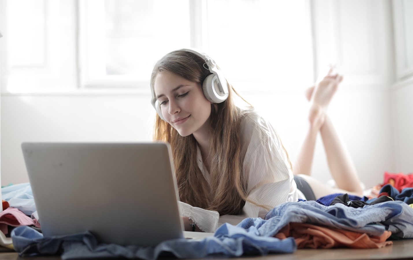 A smiling young woman wearing headphones uses her laptop to surf the web without worrying about any data caps.