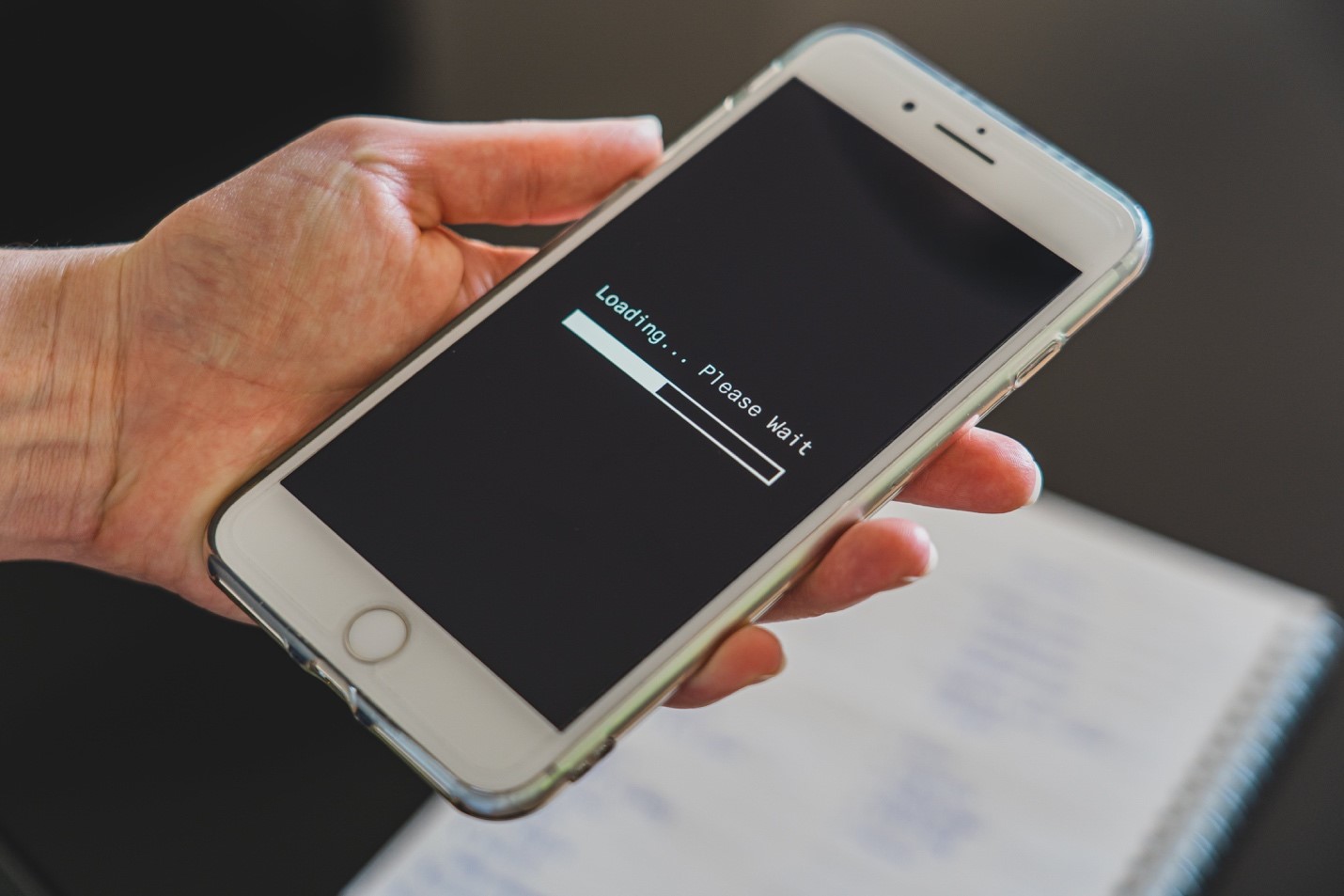 A person holds their phone out, showing a loading progress bar that is just under half-full. The person is likely frustrated with their slow Internet speeds.