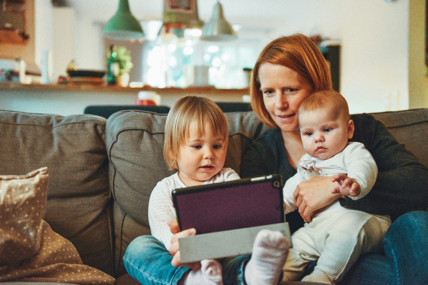 Mother with two young children sitting on a couch using a tablet, demonstrating family enjoyment and connectivity with a bundle of TV, Internet, and phone services.